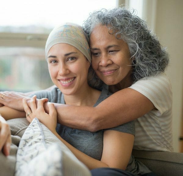 Supportive embrace between an elderly woman and a young cancer patient, symbolizing the importance of financial assistance for cancer care.