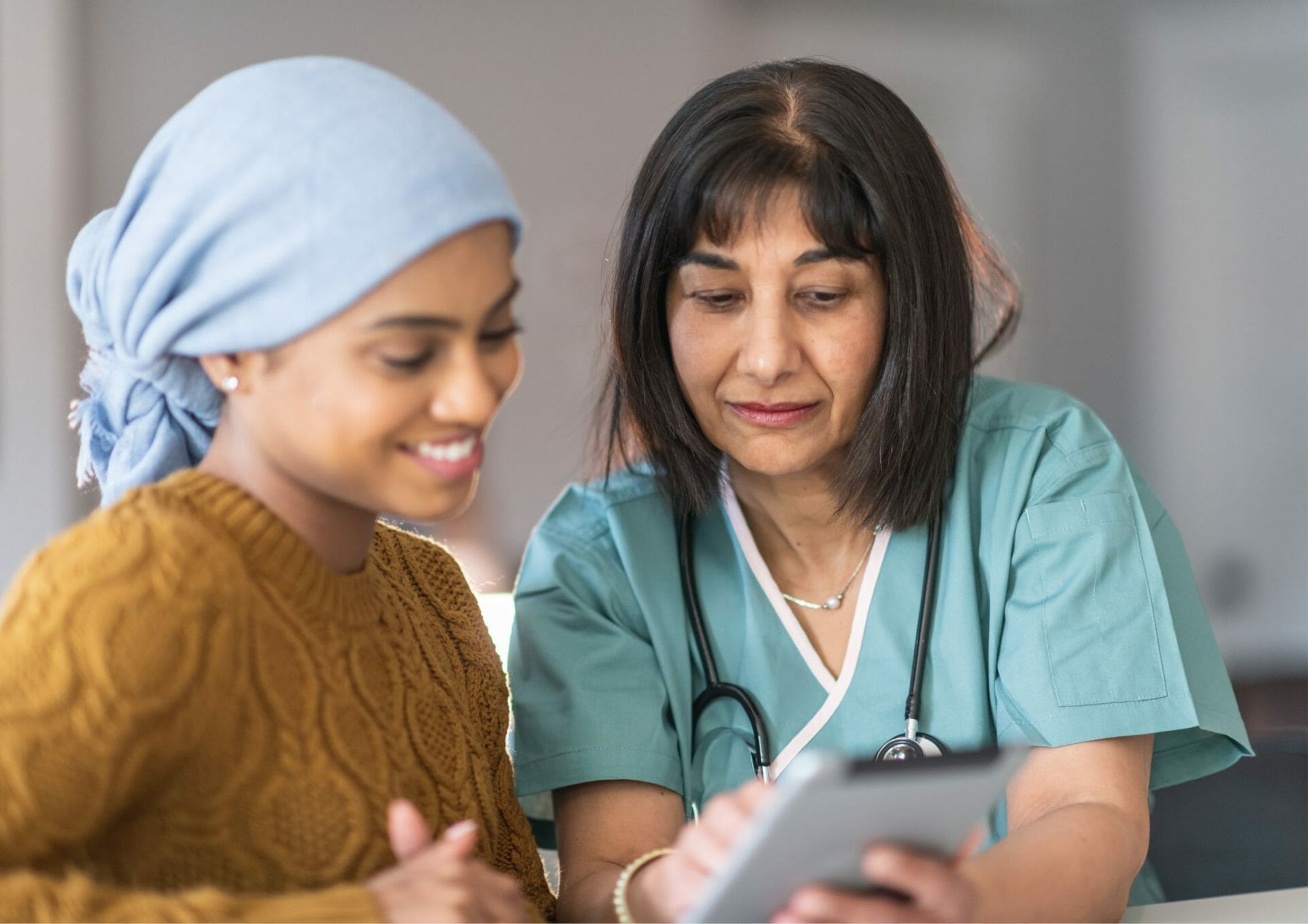Smiling cancer patient with a headscarf consulting with a doctor about financial assistance options.