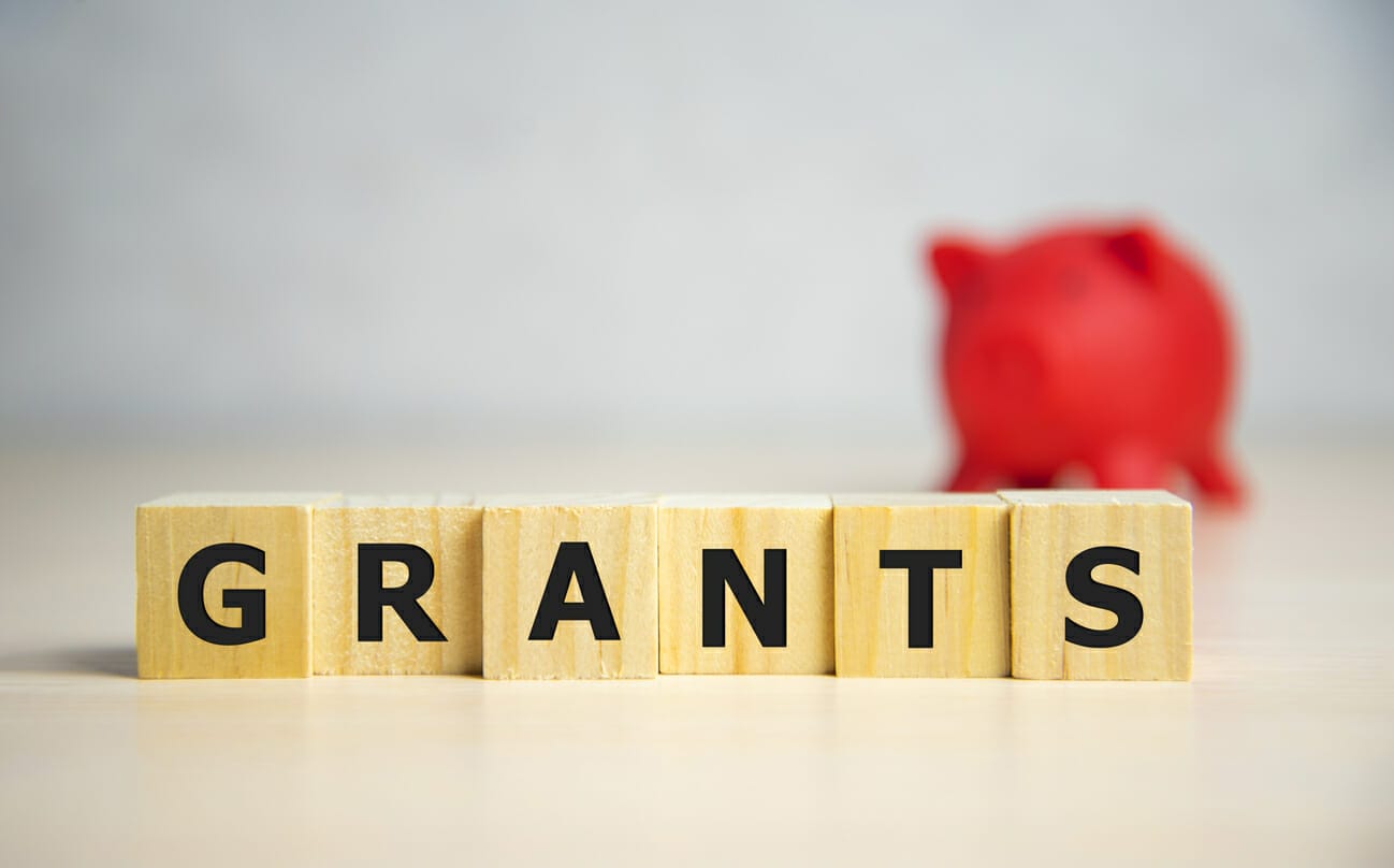 Wooden blocks spelling out 'GRANTS' with a red piggy bank in the background, representing financial aid for Myelodysplastic Syndromes (MDS) patients.