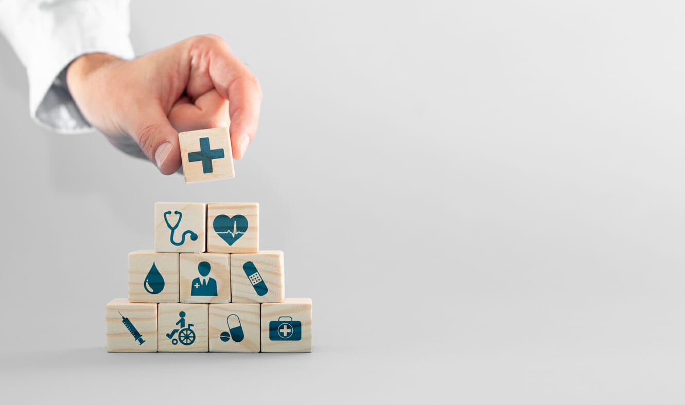 Hand placing a medical-themed wooden block on top of a pyramid, symbolizing financial assistance for cancer patients in New York.