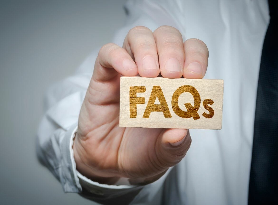 Person holding a wooden block with 'FAQs' text, indicating frequently asked questions about financial assistance in Illinois.