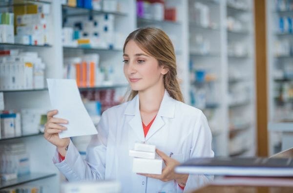 Pharmacist holding a prescription and medication boxes, representing financial assistance for leiomyosarcoma patients.