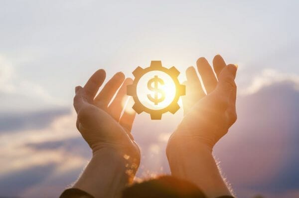 Hands holding a gear with a dollar sign against the sunlight, symbolizing financial assistance for leiomyosarcoma patients.