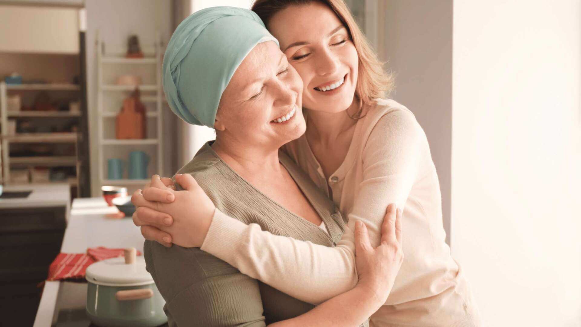 American Life Found – Smiling woman in a blue headscarf embracing her caregiver in a kitchen, highlighting support in viatical settlements
